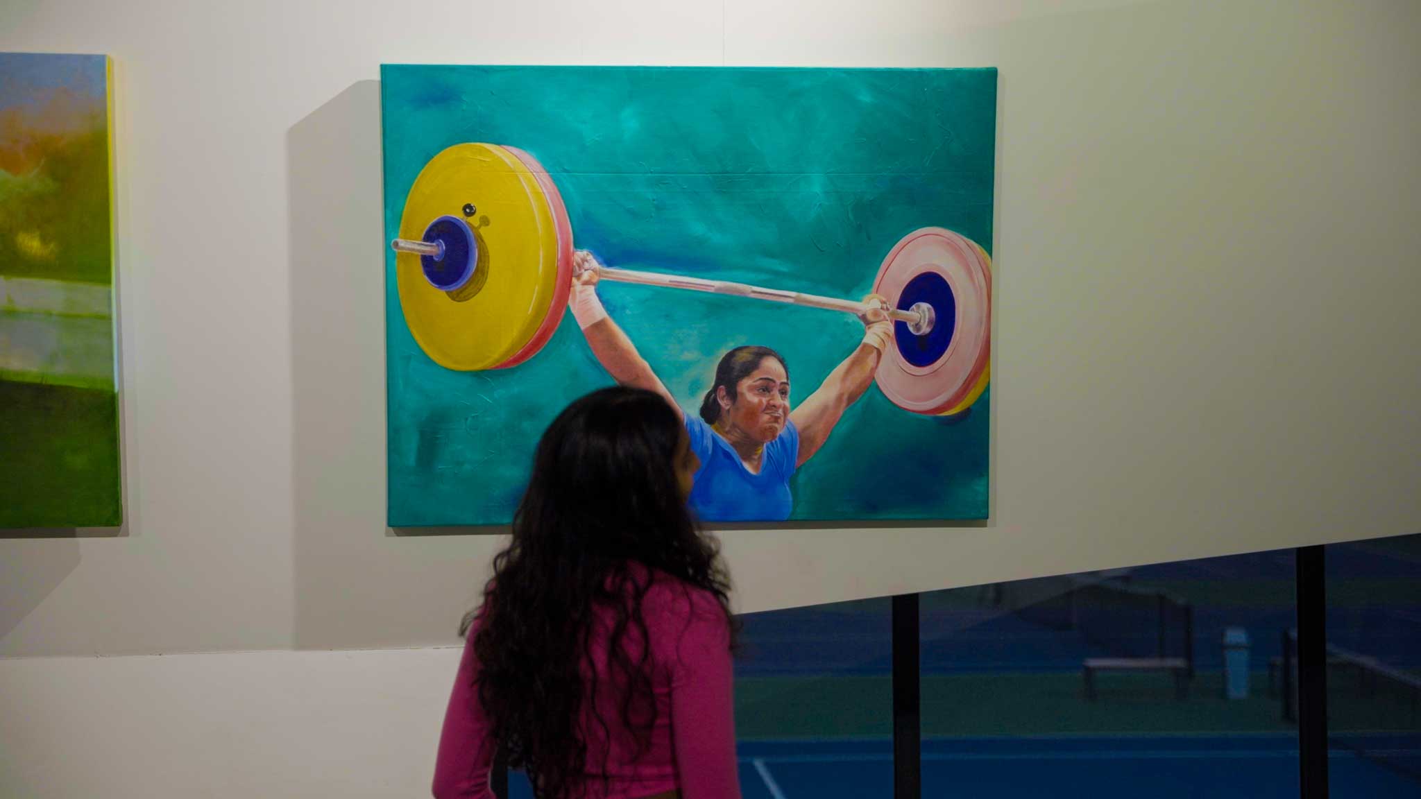 Child looking at a painting of a woman lifting weights in an art gallery